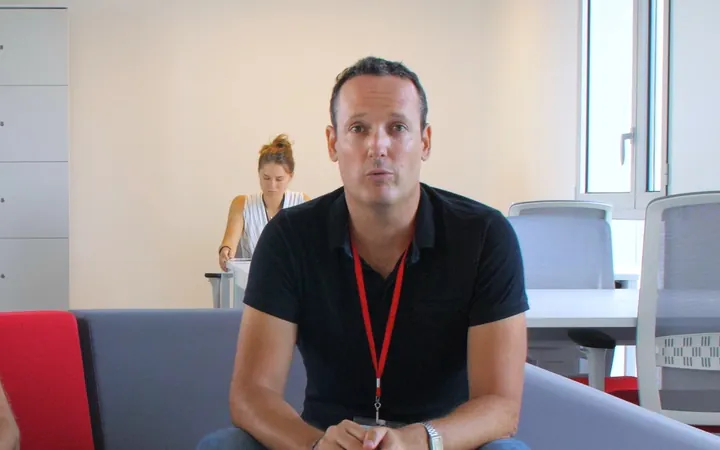 Deux hommes assis sur un canapé gris dans des bureaux, un badge autour du cou, lors d'une interview d'entreprise