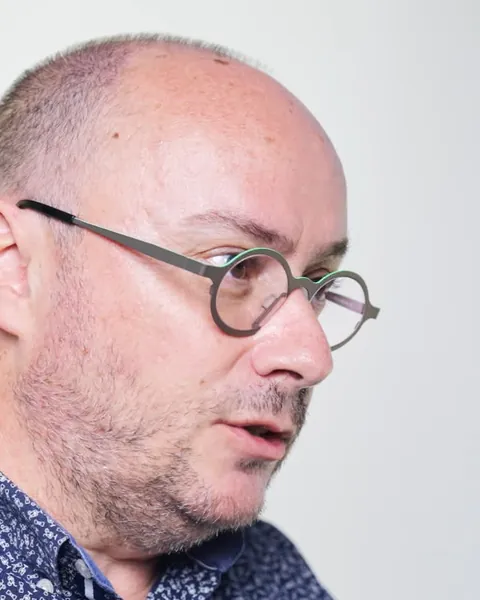 Gros plan d'un homme à lunettes qui explique un point en gesticulant, sur fond blanc